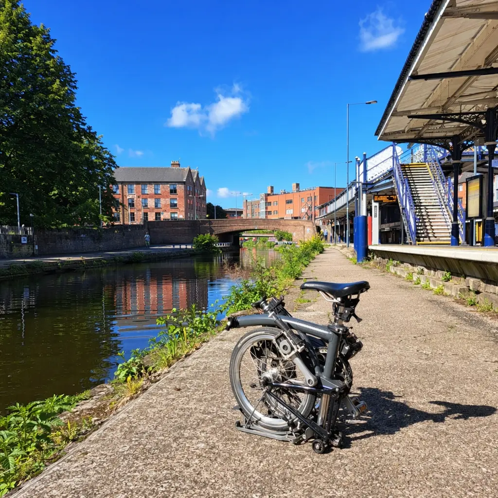 Folded bike beside a sunny canal towpath near a station