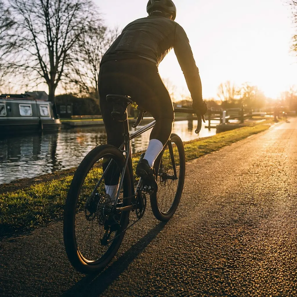 A steel all-roads bike at golden hour on a canal towpath, shown from behind with a rider silhouette.