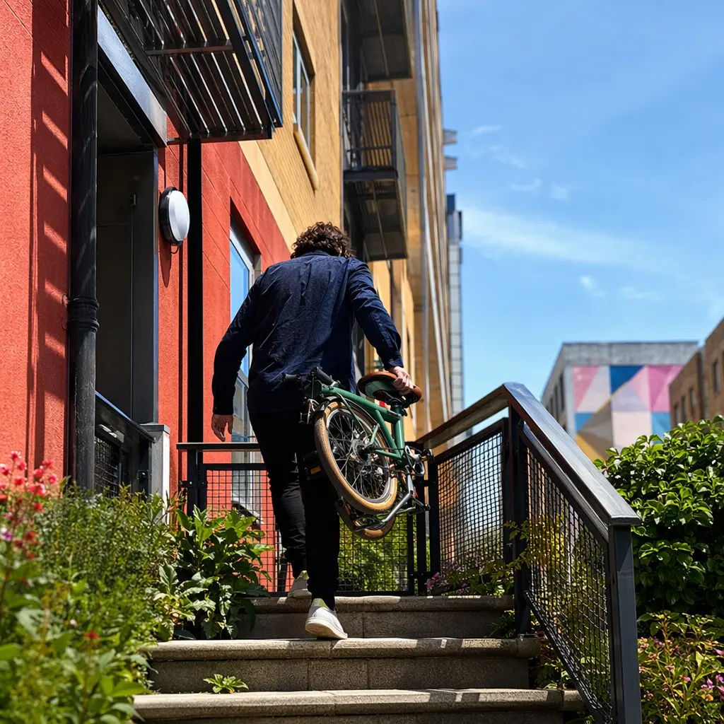 A folded bike being carried outside a small city flat on a sunny day